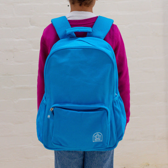 A child wearing a blue junior backpack on their shoulder, ready for school or outdoor activities.