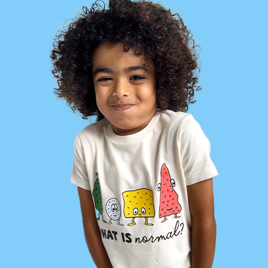 Young boy kid wearing a cream organic cotton T-shirt with "WHAT IS normal?" in white font and funny faces, smiling happily.