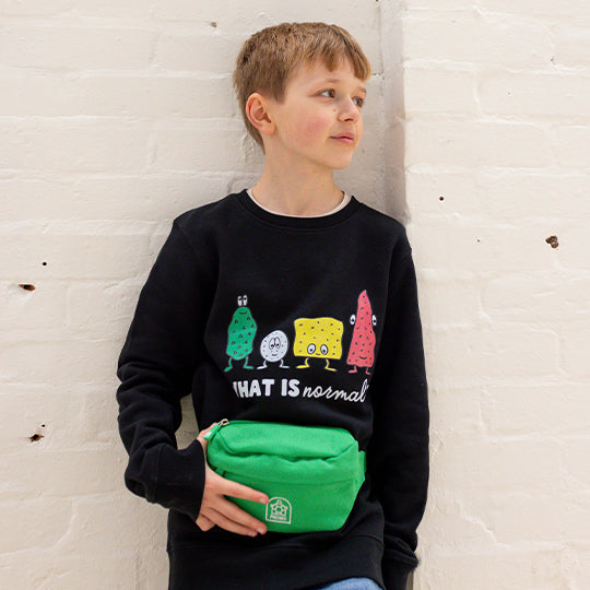 A young boy wearing a kids green bum bag around his waist, paired with black sweaters, looking stylish.