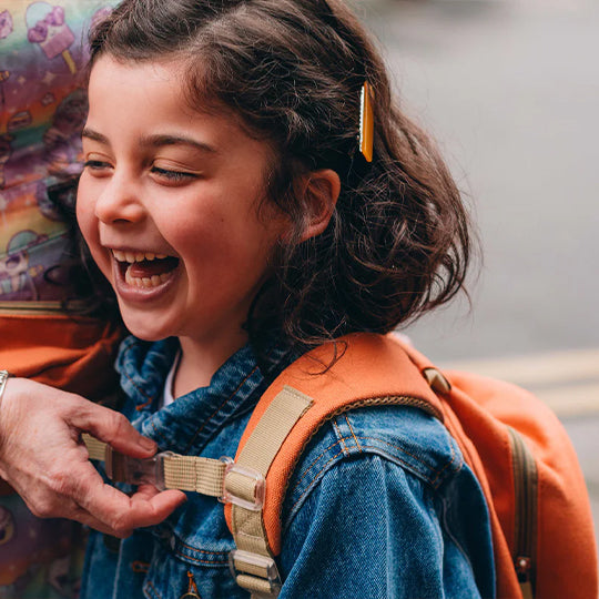 A young girl smiling while wearing an orange mini backpack from Pachee, showcasing a fun and stylish kids backpack.