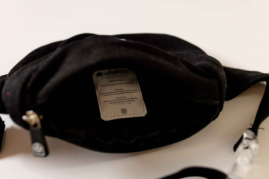 Image of a black bum bag with its main compartment open, displaying a spacious interior lined with smooth fabric and a secure zipper closure.