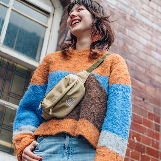 A cheerful girl wearing a crossbody neutral colour bum bag, smiling brightly, showcasing a stylish and versatile accessory for everyday use.
