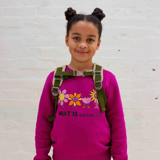 Young girl wearing a pink sweatshirt with "what is normal?" and cute flower faces printed on it.