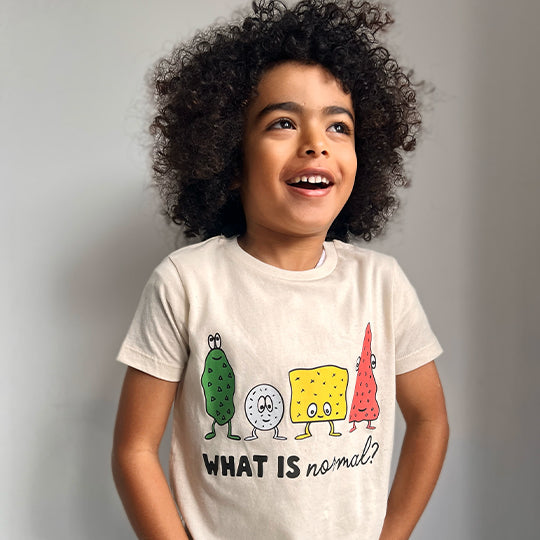 Boy wearing an organic cotton cream colour T-shirt with the statement "WHAT IS normal?" in white font, featuring funny faces.