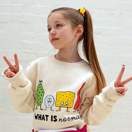 Kids cream sweatshirt made from organic cotton with "WHAT IS normal?" printed on the front with funny faces.