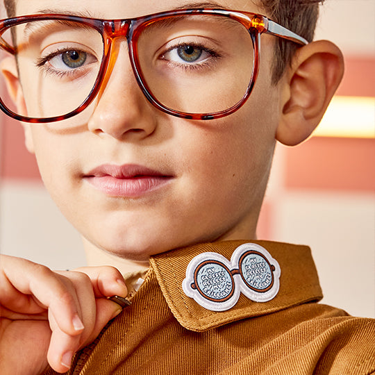 A boy wearing a shirt with the "My Glasses Patch" attached to the collar, showcasing the product.