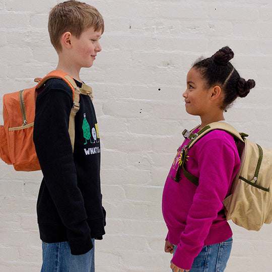 Young boy in black organic cotton sweatshirt and girl in pink sweatshirt, both wearing Pachee's mini backpacks.