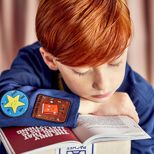 A boy wearing a "I Love to Read" patch and a "Star in the Sky" patch on his shirt, reading a book.