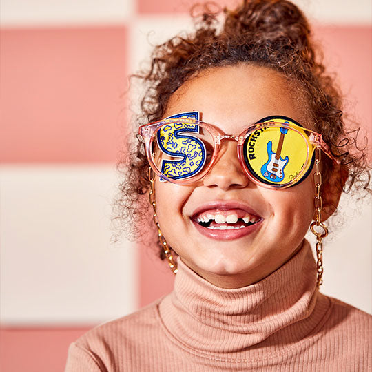 Girl wearing glasses with a Rockstar patch on one side and an alphabet "S" patch on the other side.
