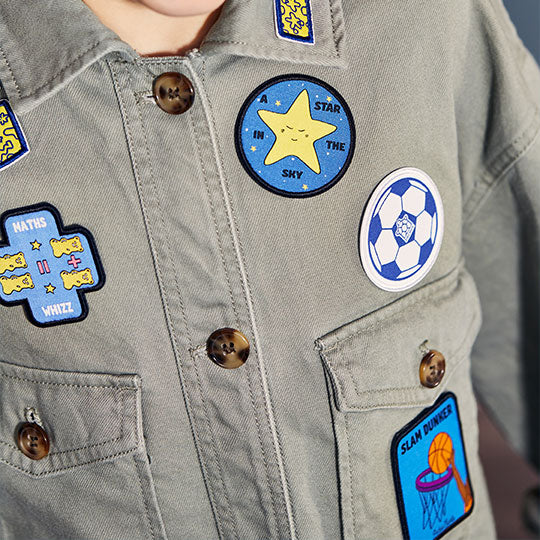 A shirt with various patches attached, including a Slum Dunker patch, Maths Whizz patch, Football patch, and A Star in the Sky patch.