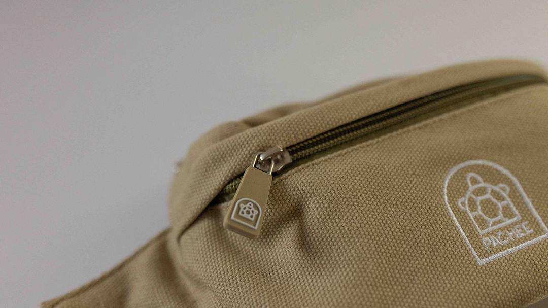 Close-up image of a brown bum bag with the front compartment's zip closed, featuring the Pachee logo prominently displayed. 