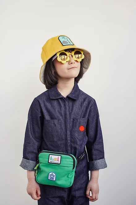 A girl wearing a hat, featuring a stick and stones patch, smiling and posing for the camera.